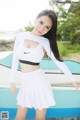 A woman in a white top and skirt posing next to a boat.