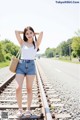 A woman standing on a train track with her hands behind her head.