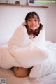 A woman sitting on a bed covered in a white blanket.