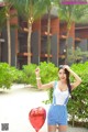 A woman holding a red heart shaped balloon in front of a building.