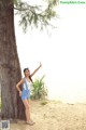 A woman standing next to a tree on a beach.