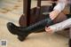 A woman in a white shirt and black boots is tying up her boots.