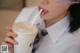 A woman in a school uniform drinking from a cup with a straw.