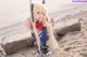 A woman with long blonde hair sitting on a rock on the beach.