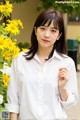 A woman in a white shirt standing in front of yellow flowers.