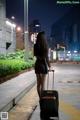 A woman walking down a sidewalk with a suitcase.