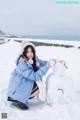 A woman kneeling down next to a snowman in the snow.