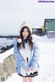 A woman in a blue jacket and hat standing in the snow.