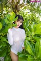 A woman in a white bodysuit posing in front of a palm tree.