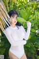 A woman in a white bodysuit posing in front of a palm tree.