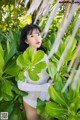 A woman in a white bodysuit standing in a lush green forest.