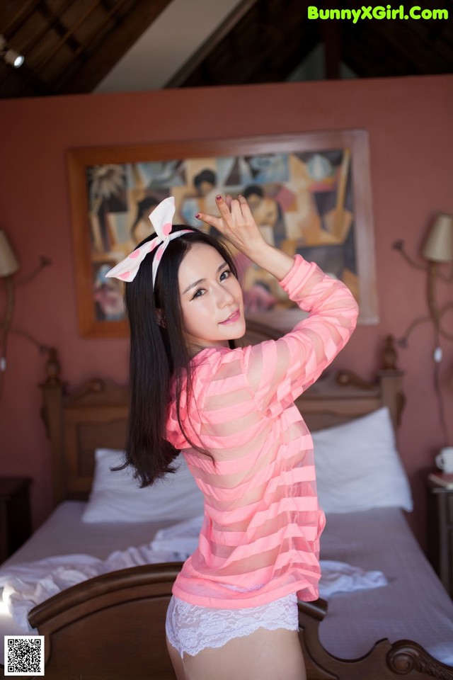 A woman in a pink shirt and white panties posing on a bed.