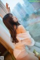 A woman in a white lingerie sitting on a window sill.