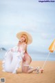 A woman in a bikini and hat sitting on the beach.