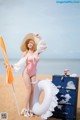 A woman in a pink bathing suit and hat standing on a beach.