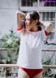 A woman in a white shirt and red panties standing on a balcony.