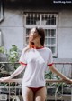 A woman in a white shirt and red panties standing on a balcony.