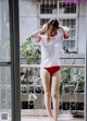 A woman in a white shirt and red panties standing on a balcony.